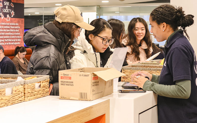 a photo of a students talking to a student staff member with food items in baskets