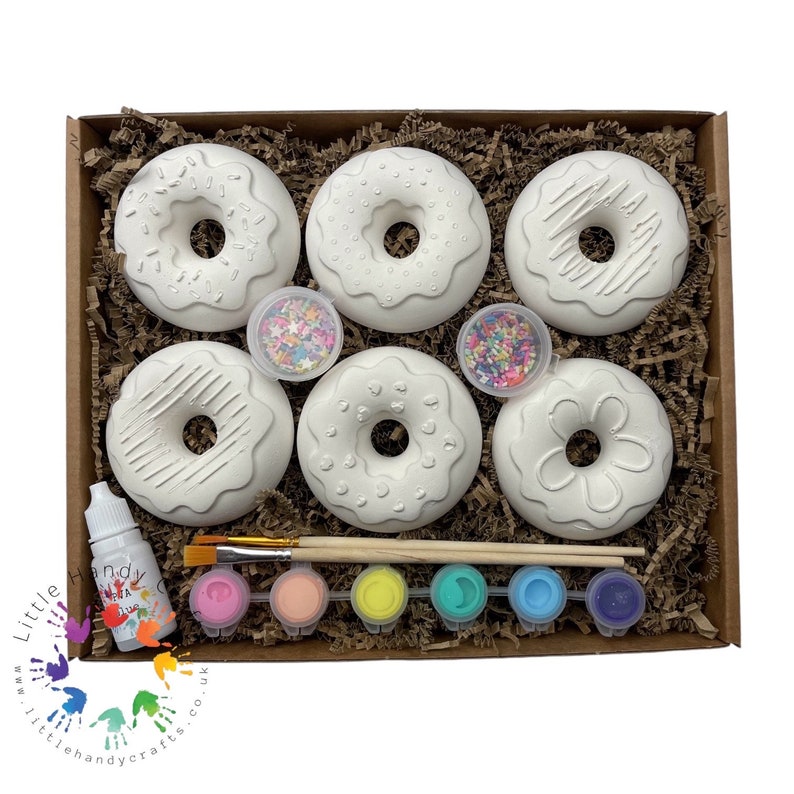 May include: A craft kit for painting doughnuts. The kit includes six white ceramic doughnuts, two paintbrushes, six small bottles of paint, two small containers of sprinkles, and a bottle of glaze.