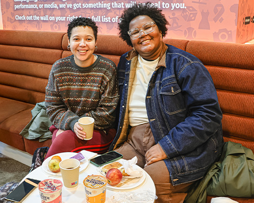2 students sat on a sofa with breakfast items on a table at the Community Breakfast